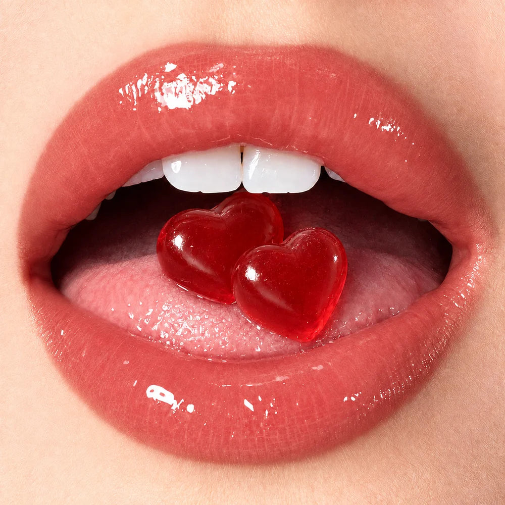 Two red heart-shaped gummies on a tongue between glossy lips